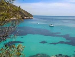 Cala con velero fondeado en mar turquesa